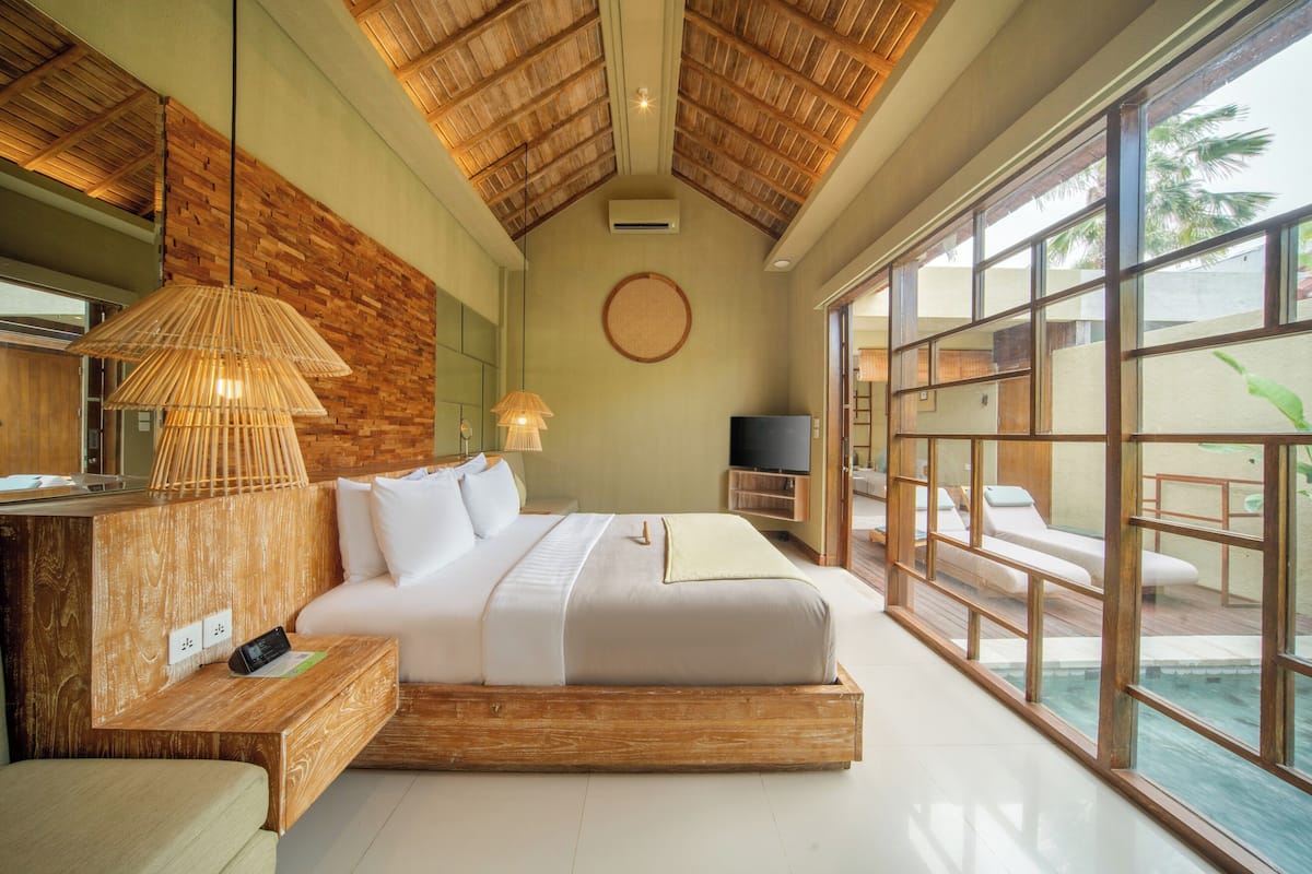 A spacious bedroom with a large bed, wooden headboard, and a view of an outdoor pool area.