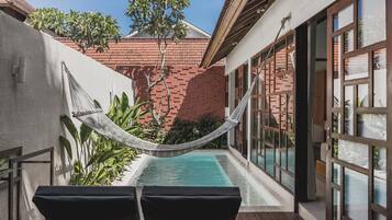 A pool area with a hammock, lounge chairs, and a view of a brick building.