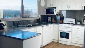 A modern kitchen with white cabinets, a microwave, a stove, and a large window offering a view. - House on the hill with Spectacular Port Bay Views (Port Campbell)