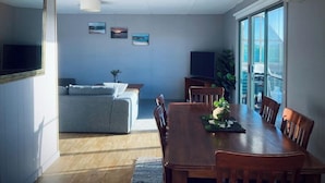 A modern living room with a sofa, a dining table with chairs, a TV, and framed pictures on the wall. - House on the hill with Spectacular Port Bay Views (Port Campbell)