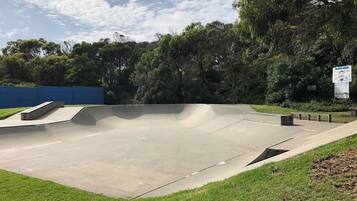 Una pista de skate con rampas de hormigón y una zona plana, rodeada de césped y árboles.