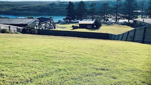 A grassy area with a building, a small structure, and a body of water in the background. - House on the hill with Spectacular Port Bay Views (Port Campbell)