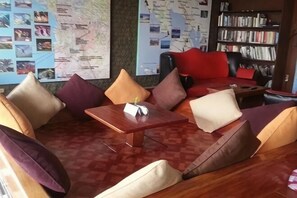 Un rincón de estar con sofás acolchados y una mesita, una estantería y una pared con un mapa y fotografías.