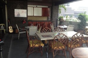 Un área de comedor al aire libre con sillas y mesas de mimbre, una guitarra y un tablero de menú.
