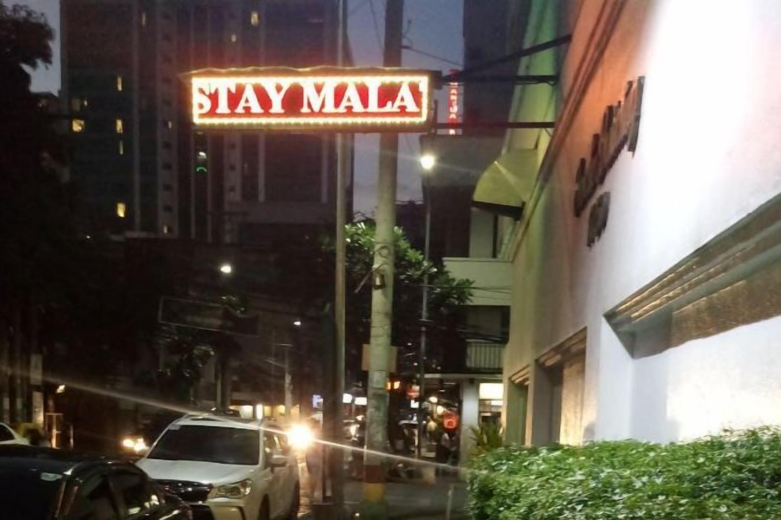 A neon sign that reads 'STAY MALA' on a building.