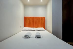 A small, single-bed room with a plain white wall and a wooden headboard. - Stay Malate (Wanderers Guest House) (MANILA)