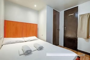 Una habitación de hotel con una cama, cabecero de madera, un armario y una puerta.