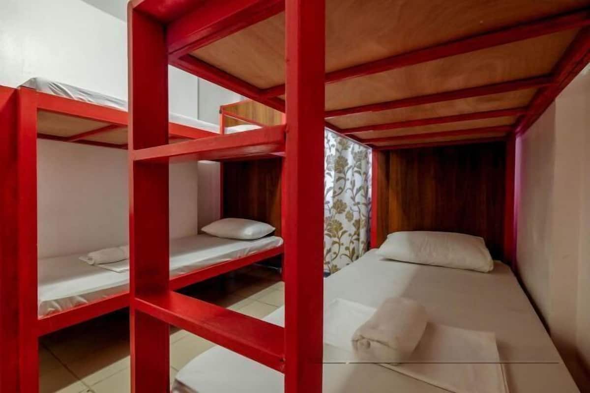 A room with bunk beds, wooden beams, and a window with patterned curtains.