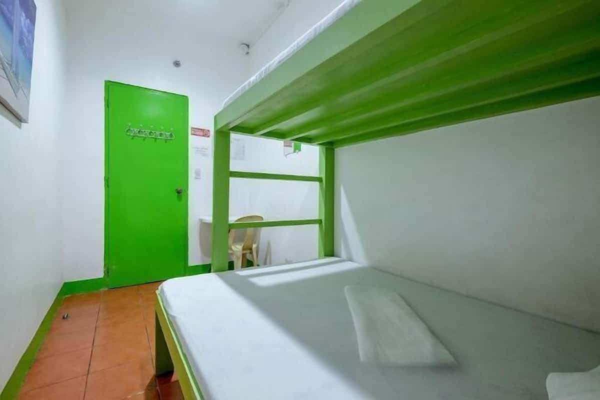 A single-bed room with a green door, white walls, and a tiled floor.