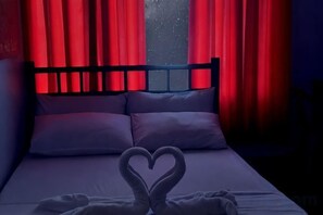 Ein Bett mit einer herzförmigen Handtuchgestaltung, roten Vorhängen und Blick auf einen sternenübersäten Nachthimmel.