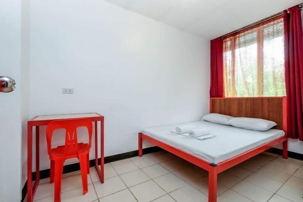A small room with a bed, a red chair, and a table.