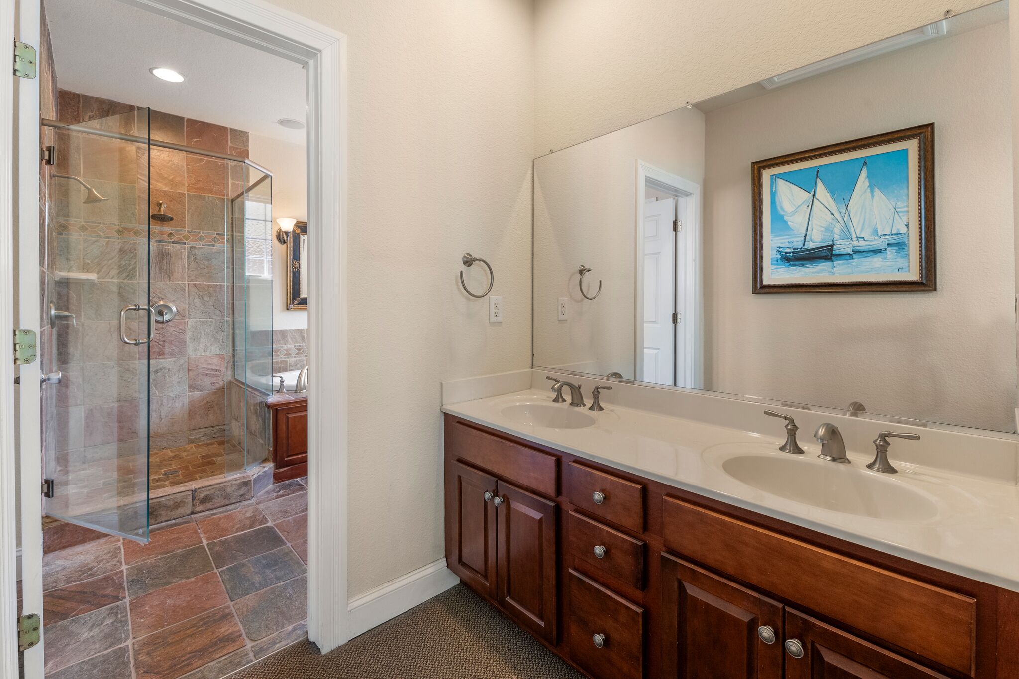 A bathroom with a glass shower enclosure, a large mirror, and a painting of sailboats.