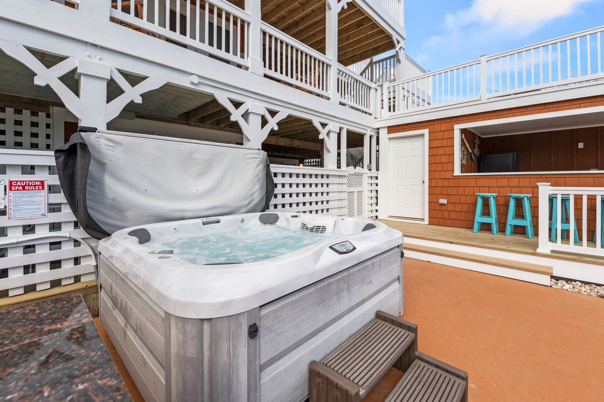 Un jacuzzi en un espacio exterior con terraza de madera y valla blanca.