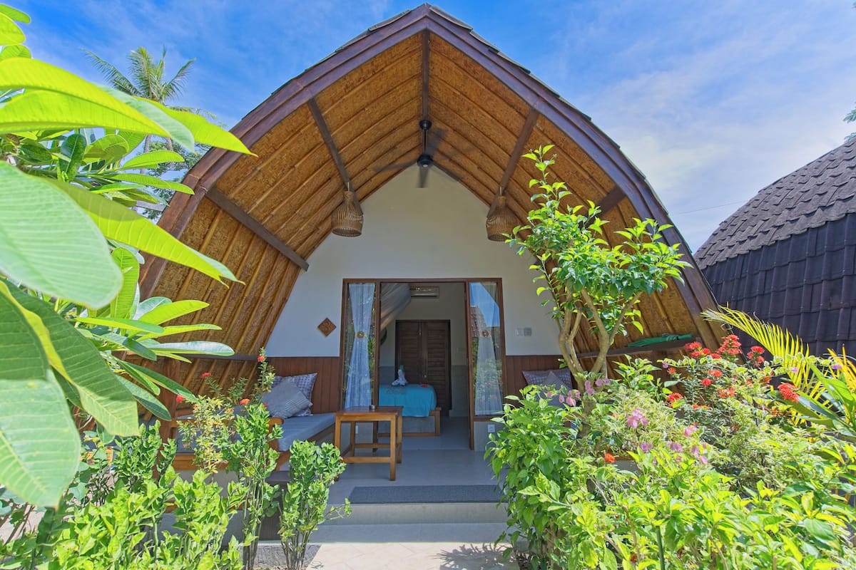 A traditional wooden house with a pitched roof, a small porch, and a bed visible inside.