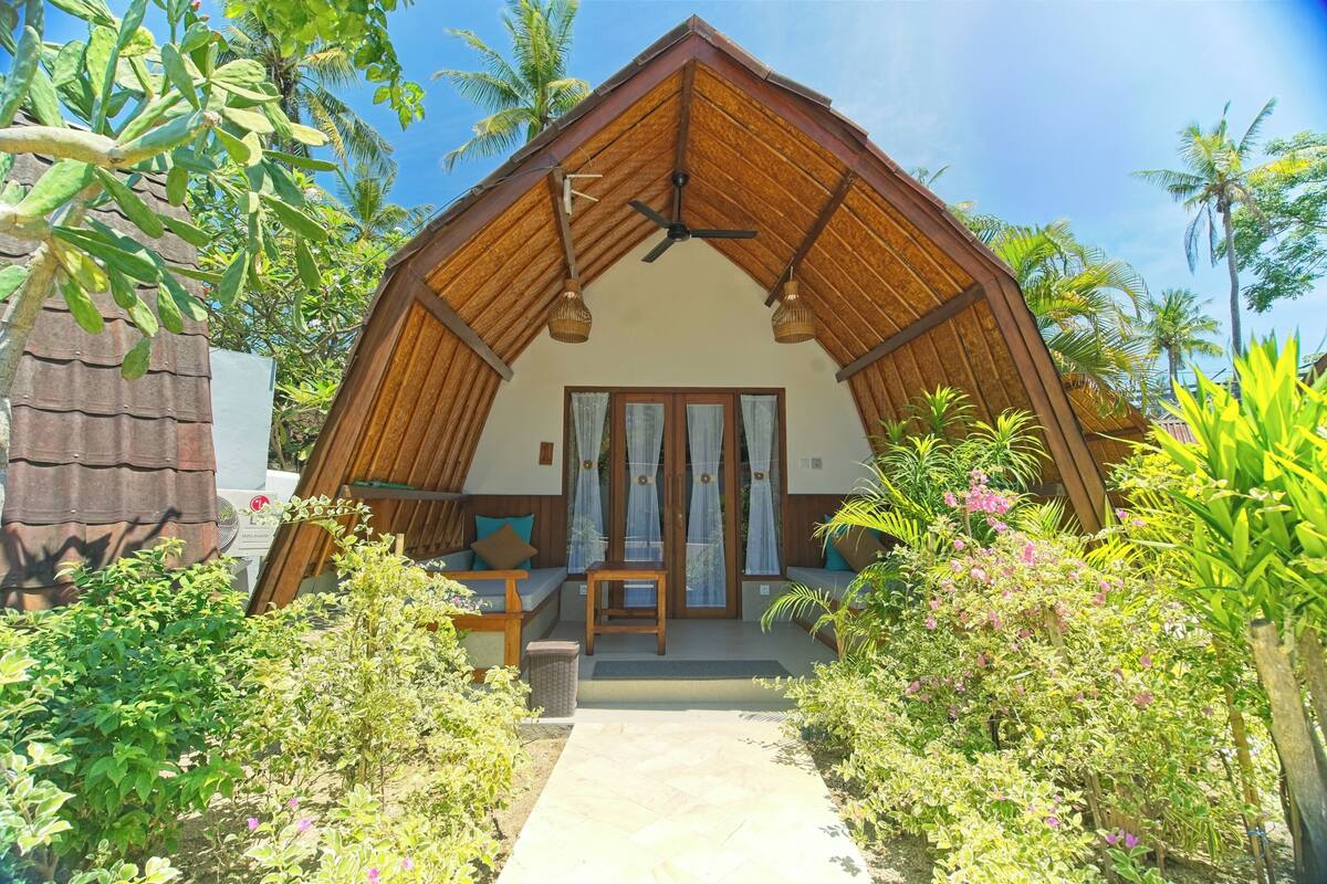 A bungalow with a sloped roof, a central seating area with a bench and cushions, and a small table.