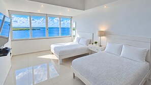 A modern hotel room with two beds, a large window with a view of the sea, and a flat-screen TV on a stand. - Beautifully Updated Modern Beachfront 4BR/3.5bth (Cancun)