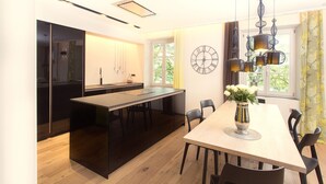 Une cuisine moderne dotée d’un îlot central, d’un coin repas avec une table en bois et d’une grande fenêtre agrémentée de rideaux.