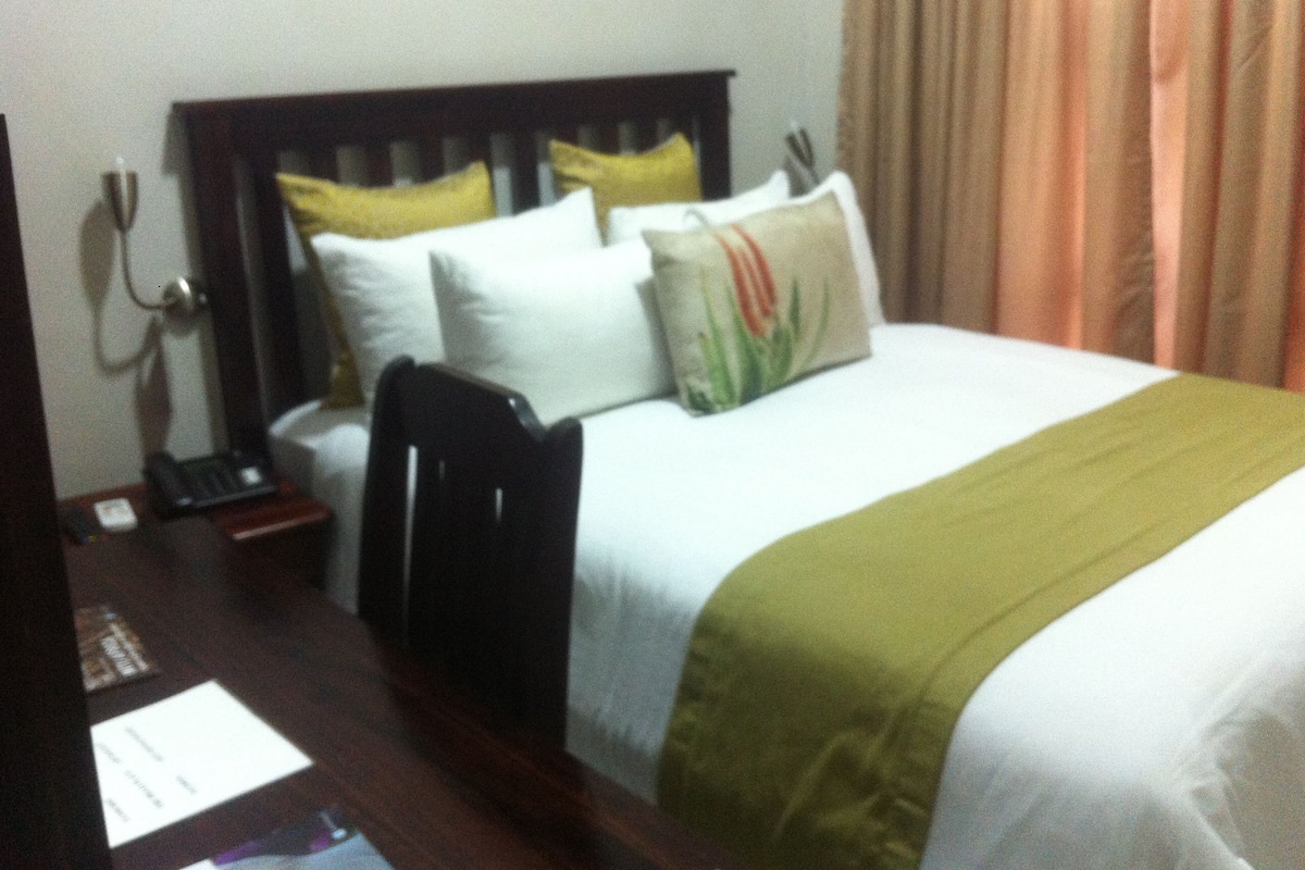A hotel room with a bed, a desk with a telephone, and a chair.