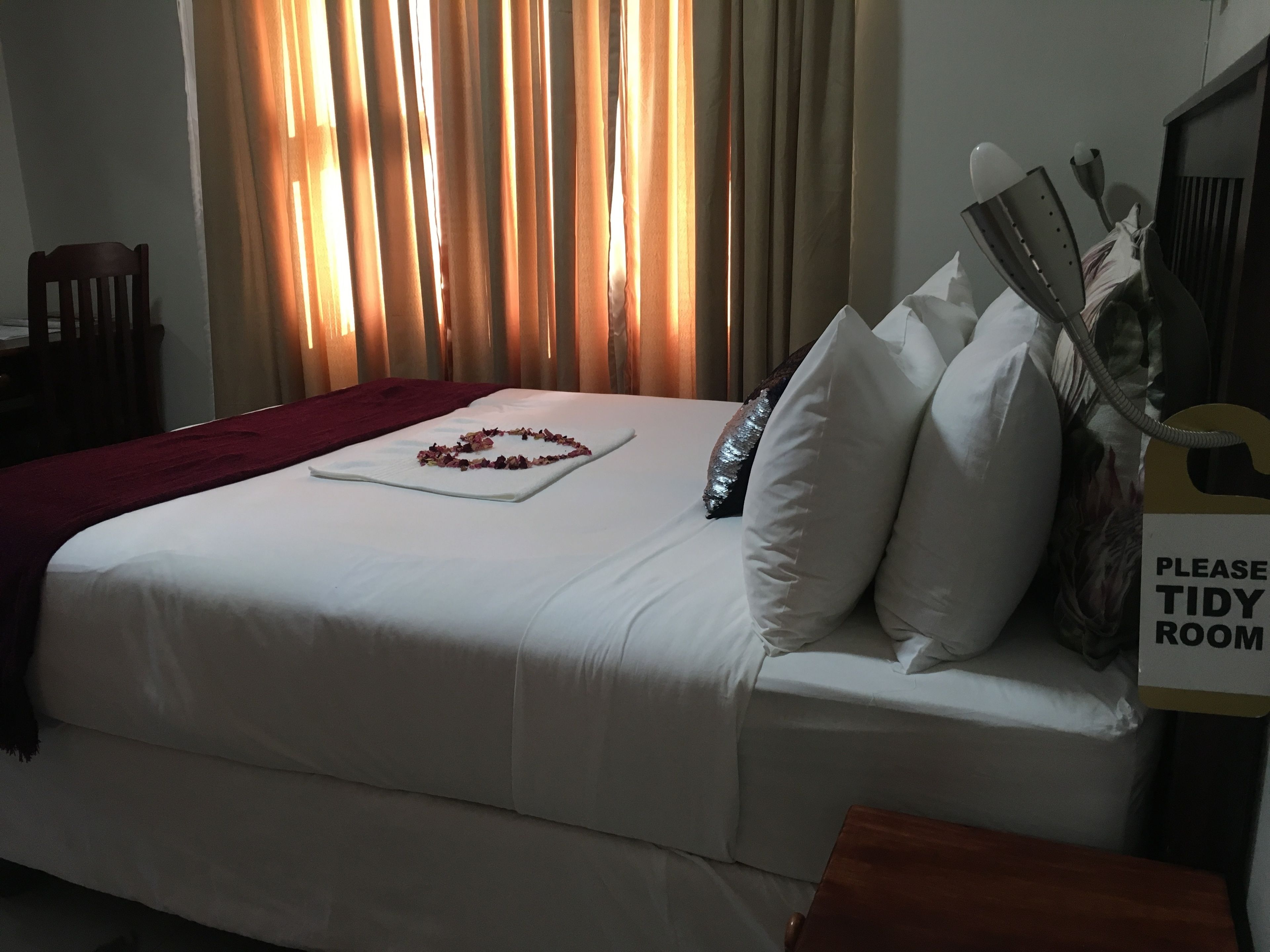 A neatly made bed with white linens, a decorative flower arrangement, and a sign requesting a tidy room.