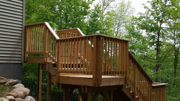 A wooden deck with a staircase leading to a platform, surrounded by rocks and trees. - Lake House - Includes 24' Pontoon, Sleeps 12, Great For Families! (Blackwell)