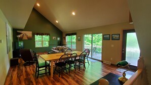 A dining area with a wooden table and chairs, a sofa, and a view of the outdoors through large windows. - Lake House - Includes 24' Pontoon, Sleeps 12, Great For Families! (Blackwell)