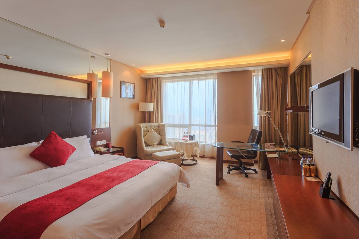 Une chambre d’hôtel avec un grand lit, un bureau, une chaise, une télévision et une fenêtre avec des rideaux.