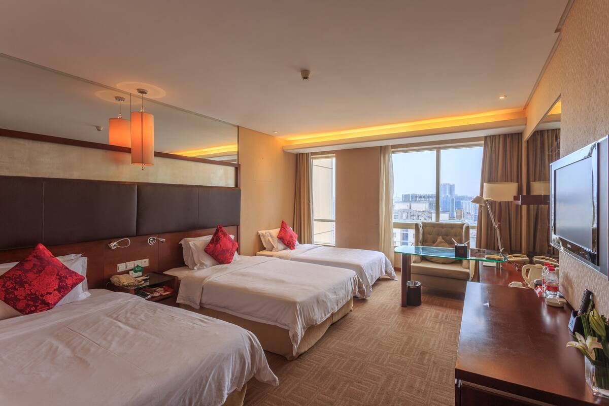 Une chambre d’hôtel avec deux lits, un bureau, une télévision et une grande fenêtre donnant sur la ville.