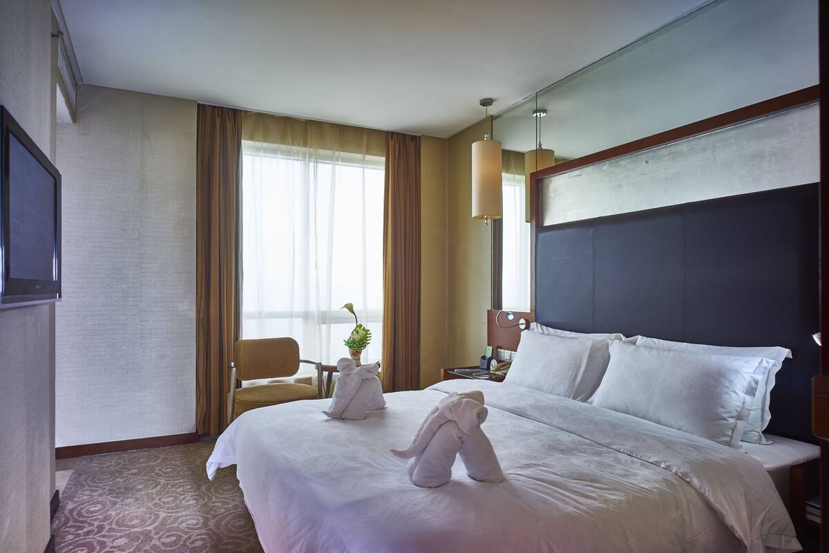 Une chambre d’hôtel avec un grand lit, un bureau, une chaise et une fenêtre avec des rideaux.