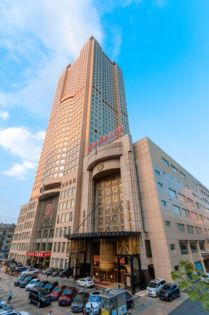 A tall hotel building with a modern design, featuring a large entrance and a parking lot with multiple cars. - Changsha Xiaoxiang Huatian Hotel (Changsha)