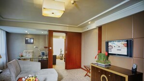 A hotel room with a sofa, a glass coffee table with fruit, a TV on a wooden cabinet, and a desk with a lamp. - Changsha Xiaoxiang Huatian Hotel (Changsha)