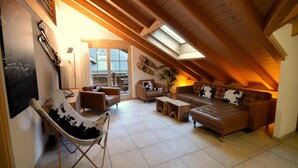 Een gezellige zolderkamer met schuine plafonds, houten balken, een bank, een fauteuil en een kleine tafel.