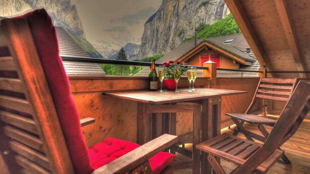 Een houten balkon met een tafel, stoelen en een fles champagne.