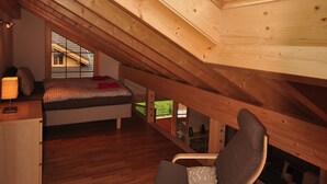 Een slaapkamer met een schuine kap, een bed, een stoel en een raam met uitzicht op een berg.
