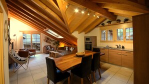 Een ruime keuken met houten balken, een eethoek met een houten tafel en stoelen, en een gezellige zithoek met een bank en fauteuils.