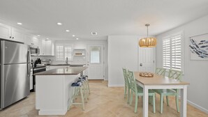 Una cocina moderna con armarios blancos, un refrigerador de acero inoxidable y una zona de comedor con una mesa de madera y sillas verdes.