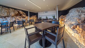 Una zona de dinar moderna amb una taula de fusta al centre i cadires al voltant, amb parets de roca amb textura de fons i il·luminació encastada al sostre.