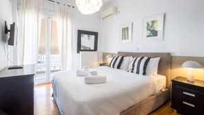 A hotel room with a bed, bedside table, lamp, artwork, and a view of the outdoors.