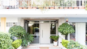 A modern building entrance with a glass door, potted plants, and a balcony with railings.