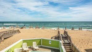 A beach view with a wooden deck and a green lounge area with white chairs. - Ocean's Edge: Oceanfront, Pool, Spa, Dogs OK (Nags Head)