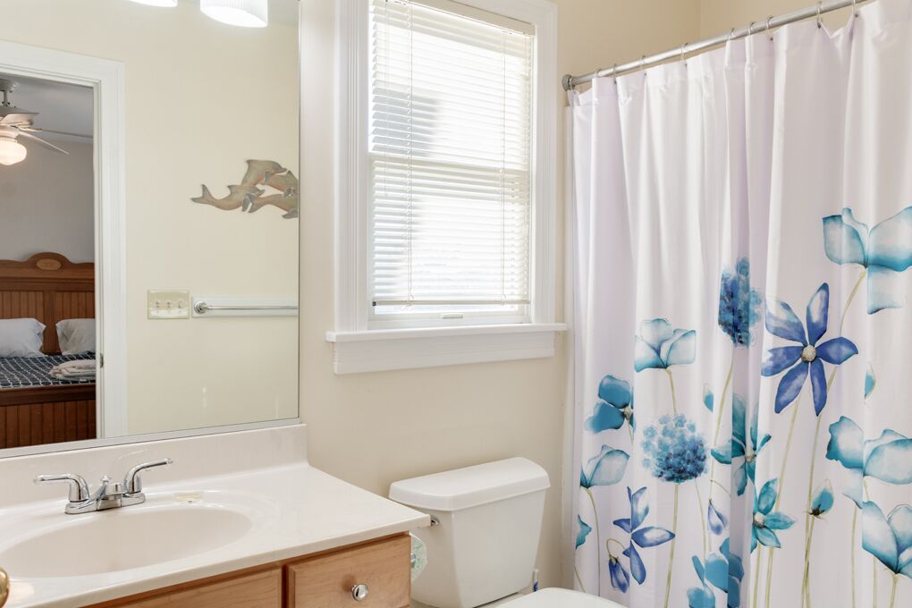 A bathroom with a white sink, a toilet, a mirror, and a window with blinds.
