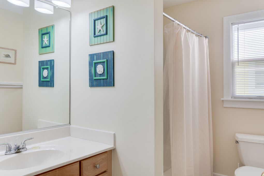 Une salle de bain avec un lavabo blanc, un meuble en bois et un rideau de douche.