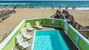 A pool area with a view of the ocean, surrounded by beach chairs and wooden walkways. - Ocean's Edge: Oceanfront, Pool, Spa, Dogs OK (Nags Head)