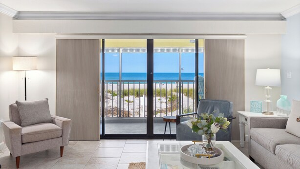 Quarto com vista para a praia, um sofá, uma cadeira e uma mesa de centro com objetos decorativos.