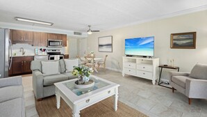 Uma sala de estar moderna com sofá, mesa de centro, TV e área de cozinha com armários e eletrodomésticos.