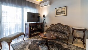 Ein Wohnzimmer mit einer Couch, einem Couchtisch, einer Bank, einem Fernseher, einem Bücherregal und einem gerahmten Bild an der Wand.