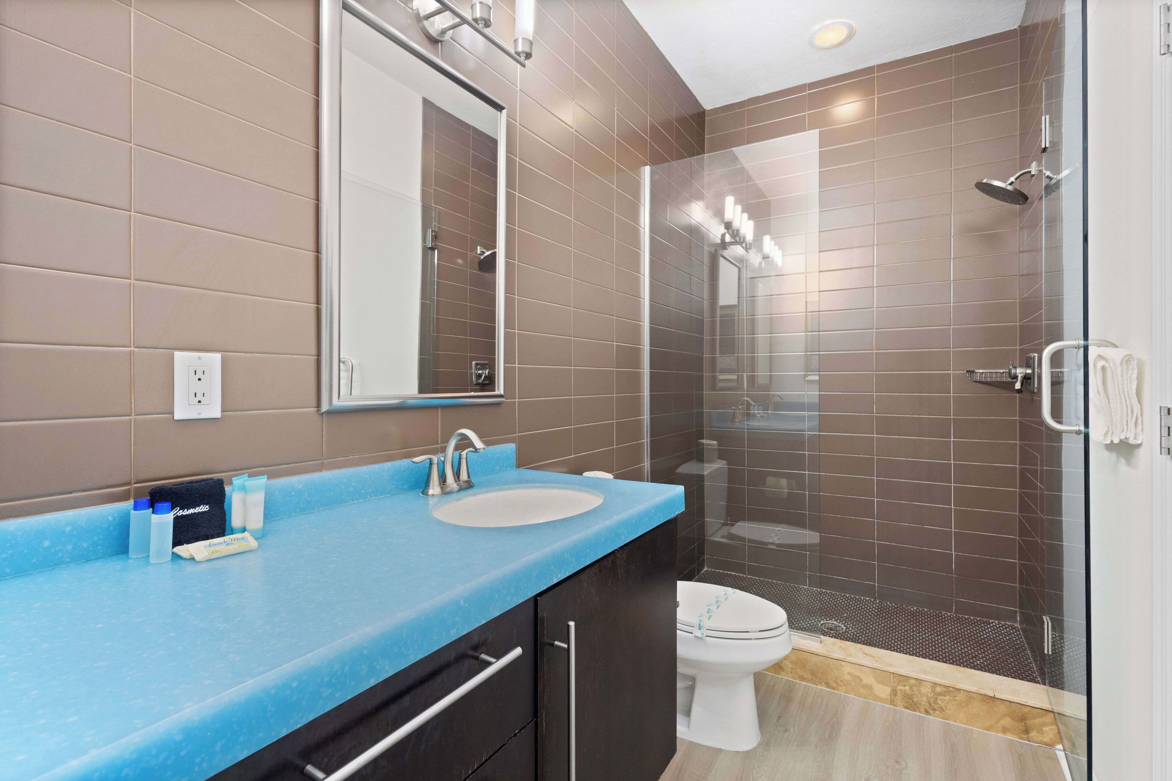 Un baño moderno con encimera azul, lavamanos blanco, ducha con cerramiento de vidrio y retrete.