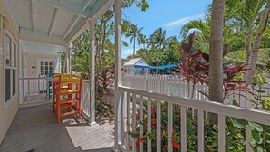 A covered porch with a white railing, wooden deck, and a small table with chairs. - Green Spot at The Truman Annex in Key West (Key West)