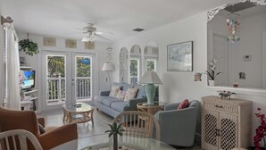 A spacious living room with a balcony, a television, and a dining area. - Green Spot at The Truman Annex in Key West (Key West)