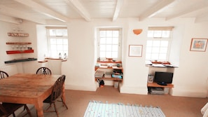 Un'accogliente sala da pranzo con un tavolo e sedie in legno, un angolo cottura con fornelli ed scaffali, e un piccolo televisore su un mobile.