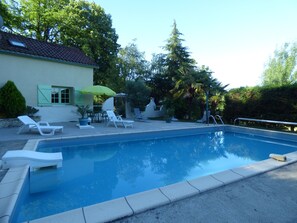 Ein Schwimmbecken mit Liegestühlen und Sonnenschirmen, umgeben von Bäumen und einem Gebäude.